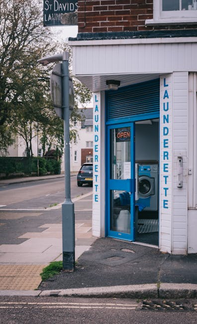 Exterior view of a small laundrette on Tufnell Park Road operated by Carpet Cleaners N7, featuring a white wooden façade with blue vertical signage reading 'LAUNDERETTE' on both sides of the entrance